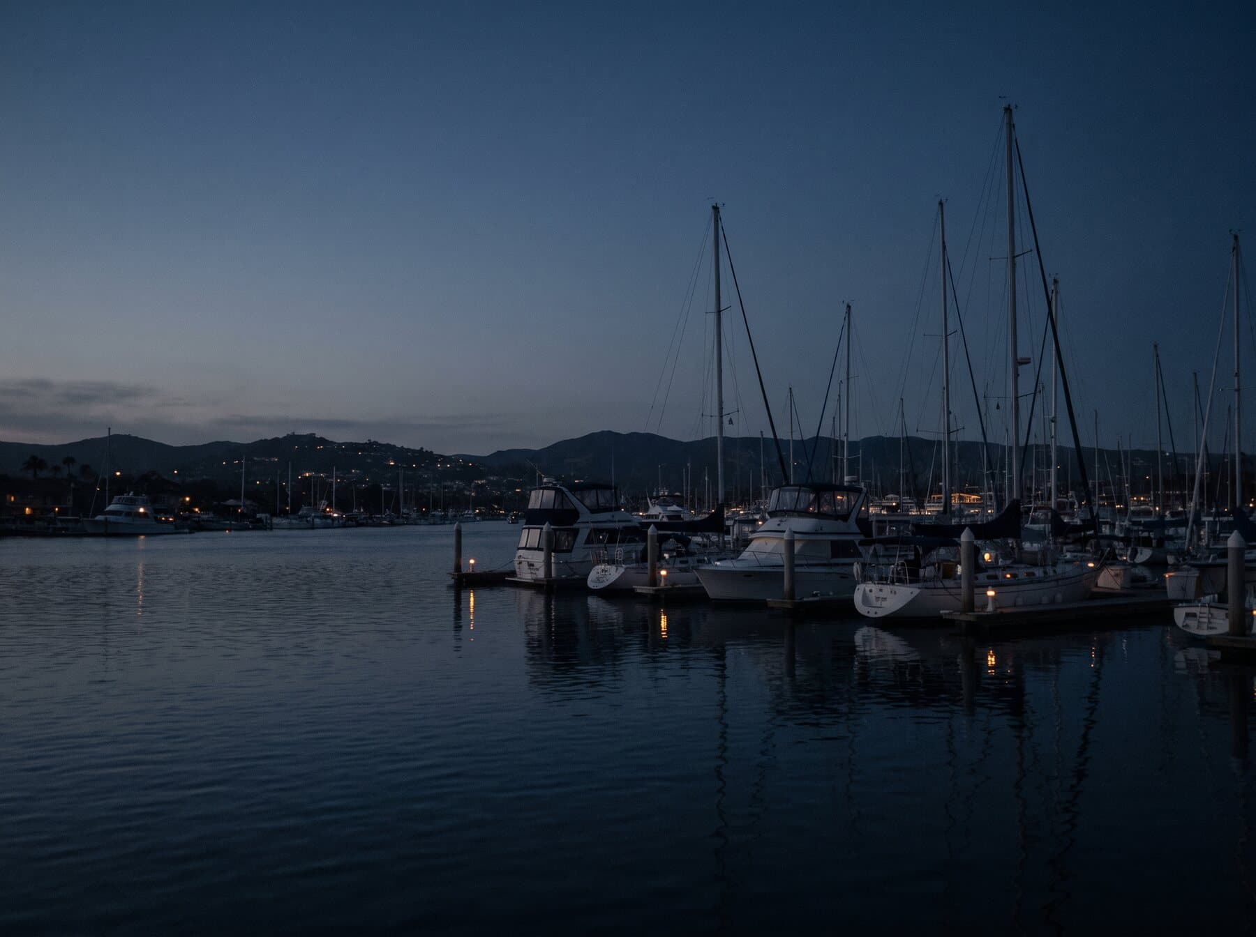 Newport Harbor at dusk, moored boats and dock lights on still water